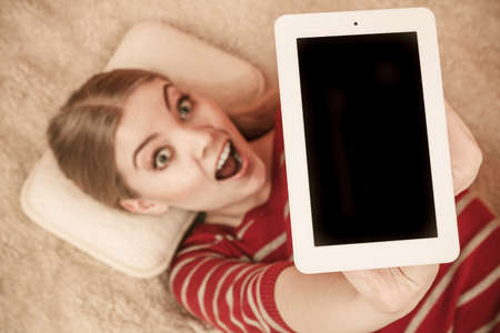 Woman laying and holding tablet computer with blank screen showing copyspace. Happy smiling woman advertising new modern technology.の写真素材