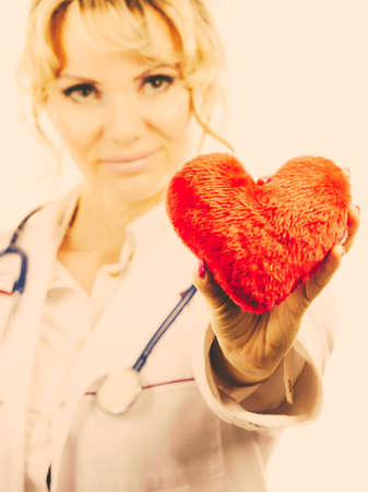 Love from working and helping people. Mid age blonde doctor in white medical apron with heart. Enjoy work concept. Filtered.の写真素材
