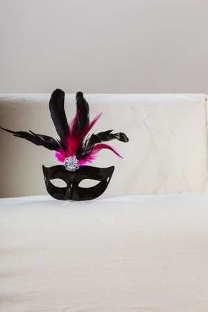 Holidays and celebration concept. Black pink color carnival venetian mask laying on couch at homeの写真素材