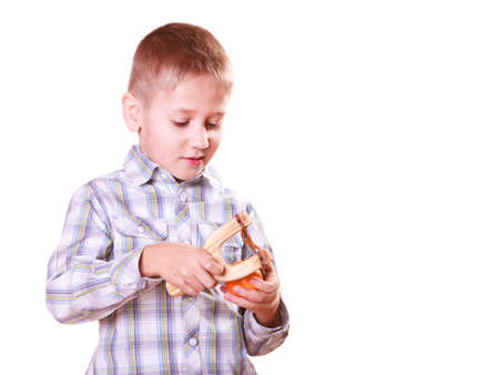 Nature and free time prankster little boy. Child have fun with  wooden sling shot and fruit hold mandarine.の写真素材