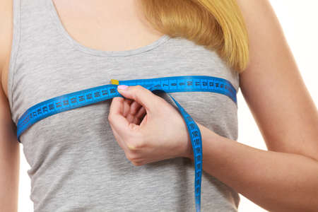 Closeup of female body. Fitness woman fit girl with measure tape measuring her chest breasts isolated on whiteの写真素材