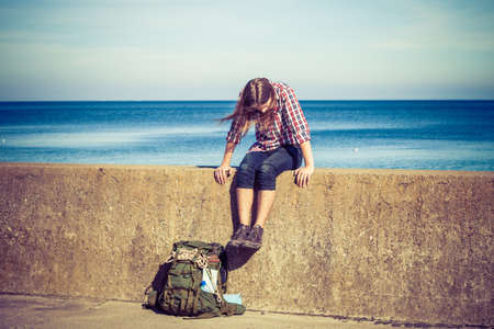 Man tourist backpacker relaxing outdoor by sea shore sitting on grunge wall. Adventure, summer, tourism active lifestyle. Young hipster guy trampingの写真素材