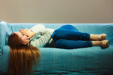 Loneliness negative emotion concept. Young sad stressed woman lying on couch at homeの写真素材