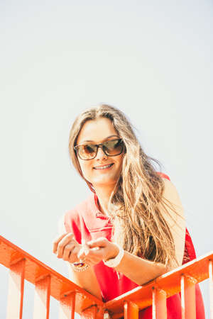 Young long haired girl with sunglasses leaning against railing on the urban bridge. Lifestyle funky in summer. Trendy cool sport teen.の写真素材