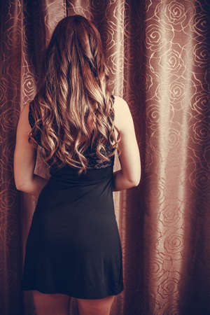 Sexy seductive woman by curtain. Sensual girl with long hair in lingerie. Female fashion. Back rear view.の写真素材