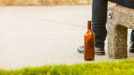 Man depressed with wine bottle sitting on bench outdoor. People abuse and alcoholism problems.の写真素材
