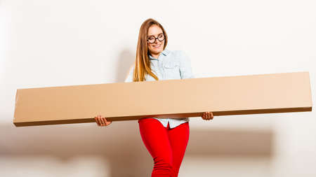 Happy woman moving into new apartment house carrying carton box with furniture. Young girl arranging...