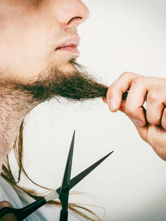 Cut and shave concept. Young man with long beard holding scissors. Part face boy cutting hair on...