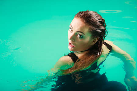 Sexy seductive woman wearing black dress in swimming pool water. Young attractive alluring girl...