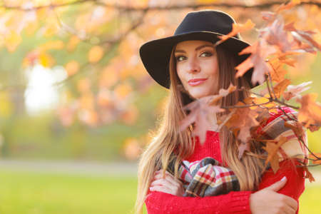 Portrait of attractive young smiling woman in autumnal park. Fashionable girl wearing red sweater scarf and black hat.の写真素材