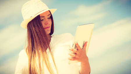 Technology enjoyment. Long haired beauty girl in straw hat with tablet e-book on beach. Student...