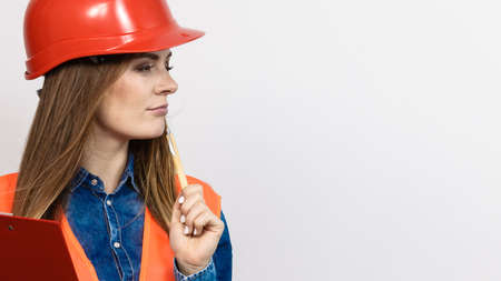 Woman construction worker builder structural engineerin in orange vest red hard helmet holds pen file pad. Safety in industrial work. Studio shotの写真素材