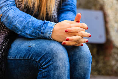 Hands gesture. Woman wearing jeans waiting for someone sitting on bench. Part body nervous shy girl outdoor in park.の写真素材