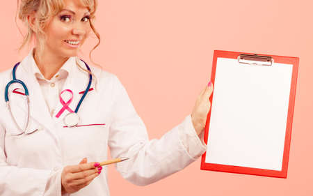 Diagnosis concept. Middle aged female doctor with pen showing red empty folder with pink breast cancer awareness ribbonの写真素材