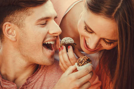 Love and happiness. Cute lovely lovers feeding each other by cupcakes cookies. Smiling couple with sweet food having fun.の写真素材
