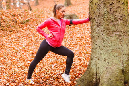 Sport and recreation. Fit slim sporty girl stretching warming up outdoor in autumnal park forest. Woman exercising on fresh air.の写真素材