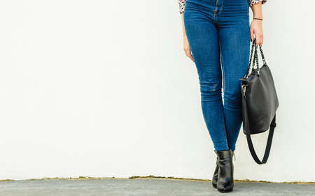 Autumn fashion outfit. Fashionable woman long legs in denim pants black stylish high heels shoes and handbag outdoor on city streetの写真素材