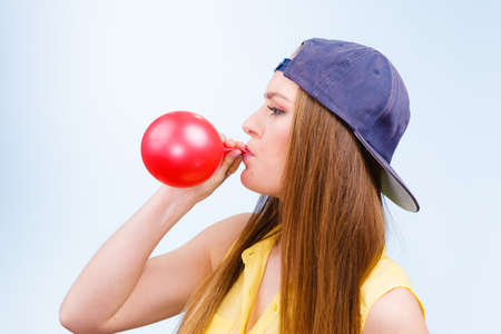 Teens and parties. Preparation for celebration. Trendy teenage girl blowing red balloon. Young beauty woman prepare accessories for party.の写真素材