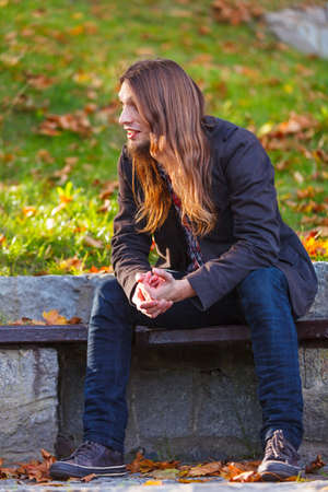 Man long hair sitting on bench outdoor in autumnal park, relaxationの写真素材