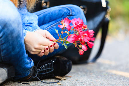 Lifestyle and leisure. Part body woman with beautiful pink flower sitting on ground. Modern fashionable girl wearing jeans clothes spends time on fresh air.の写真素材