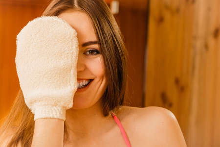 Funny young woman in wood finnish spa sauna with exfoliating glove. Girl in bikini relaxing. Skin care concept.の写真素材