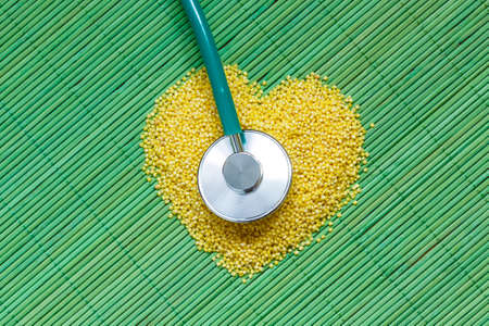 Dieting healthy living concept. Millet groats heart shaped and stethoscope on green mat surface.. Healthy food help lower cholesterol.の写真素材