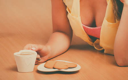 Closeup of girl with heart shape gingerbread cookies and tea or coffee at home. Retro woman with hot beverage relaxing in kitchen.の写真素材