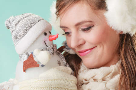 Smiling pretty cute woman holding little snowman. Attractive girl in earmuffs and scarf in studio on green. Winter fashion.の写真素材