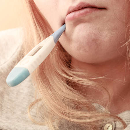 Sick ill woman with digital thermometer in mouth. Young girl having high fever measuring temperature. Health.の写真素材