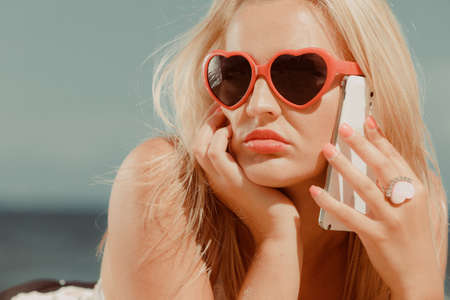 Young girl on beach with sunglasses talking using cellular phone. Communication and internet concept.の写真素材
