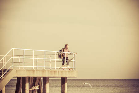 Man hiker backpacker on pier. Young guy tramping with backpack by seaside. Adventure and tourism. Beautiful sea landscapeの写真素材