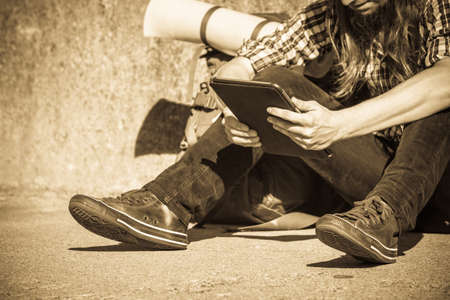 Man tourist backpacker relaxing outdoor sitting by grunge wall using tablet. Internet, tourism active lifestyle. Young hipster guy trampingの写真素材
