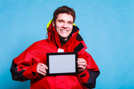 Young male with tablet. Man in waterproof clothes holding device. Adventure danger technology...