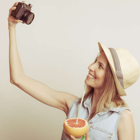 Happy tourist woman in straw hat taking selfie self picture with camera while holding grapefruit...