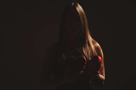 Valentine day. Woman in black holding heart box gift present. Elegant attractive model with valentines symbol sign. Studio shot.の写真素材