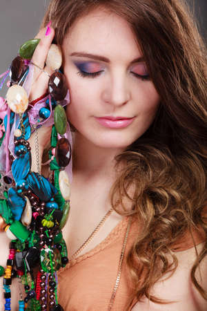 Pretty young woman holding many plentiful of precious jewelry necklaces beads. Portrait of gorgeous fashion girl in studio on gray.の写真素材