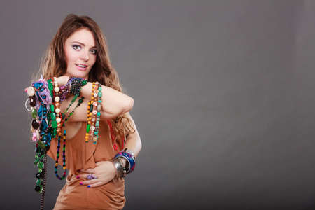 Pretty young woman wearing bracelets and rings holding many plentiful of precious jewelry necklaces beads. Portrait of gorgeous fashion girl in studio on gray.の写真素材