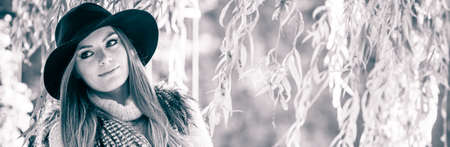 Lovely cute gorgeous woman wearing black hat fur waistcoat sweater posing around leaves of willow...