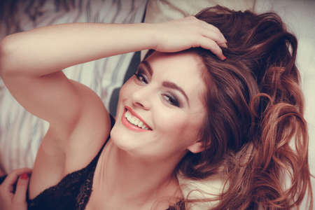 Portrait of happy seductive woman wearing lingerie in bed at home. Attractive sensual smiling young girl with long hair. Female underwear fashion.の写真素材