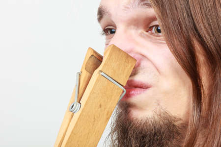 Man with clothespin clip peg on his nose. Young long haired guy feeling unpleasant odor stink. Bad...