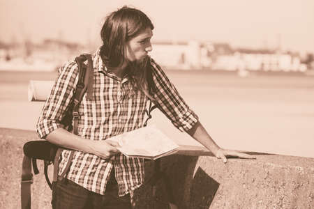 Man hiker backpacker with backpack by seaside reading map searching looking for direction guide. Adventure, tourism active lifestyle. Young long haired guy trampingの写真素材