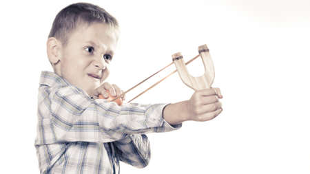 Children upbringing problems. Kid holding slingshot in hands. Bad naughty boy shoots from a wooden sling on whiteの写真素材