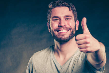 Portrait of happy smiling handsome man guy giving thumb up gesture in studio on black. Success.の写真素材