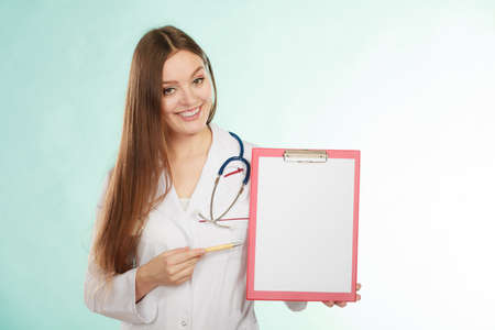 Results and information of treatment. Young female doctor holding empty folder with files of desease illness. Specialist point by pen blank clipboard. Woman in medical uniform with stethoscope.の写真素材