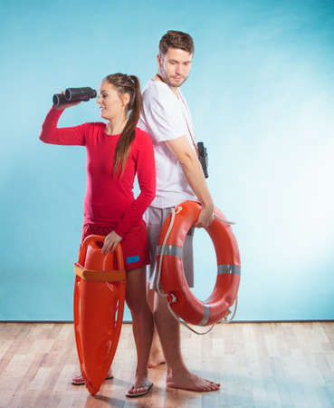 Lifeguards with rescue tube and ring buoy lifebuoy. Man and woman supervising swimming pool with binoculars on blue. Accident prevention.の写真素材