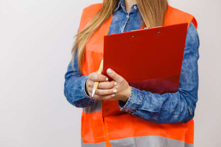 Woman construction worker builder structural engineerin in orange vest holds pen file pad. Safety in industrial work. Studio shotの写真素材