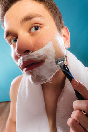 Young man shaving using razor with cream foam. Handsome guy removing face beard hair. Skin care and hygiene.の写真素材