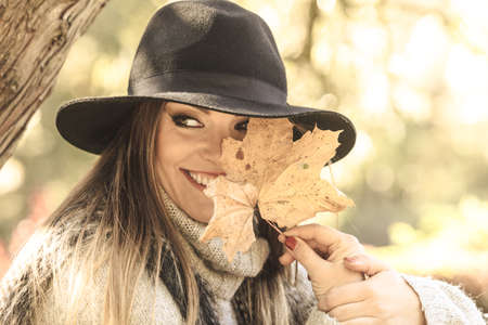 Seasonal specific. Gorgeous lovely young girl holding gold brown leaf. Beauty trendy woman spending time in autumnal park.の写真素材