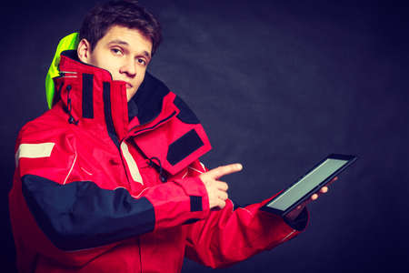 Young man using tablet. Male in windproof waterproof clothing. Internet connection adventure danger outdoors concept.の写真素材