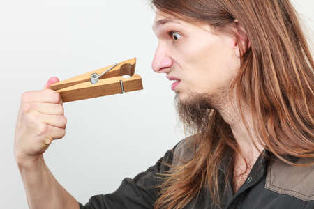 Unpleasant bad smell concept. Portrait of young long haired man with clogged nose by big clothespin.の写真素材